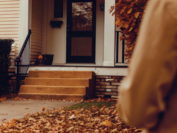 Dilapidated house entrance with scattered fall leaves.