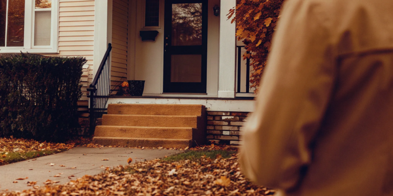 Dilapidated house entrance with scattered fall leaves.