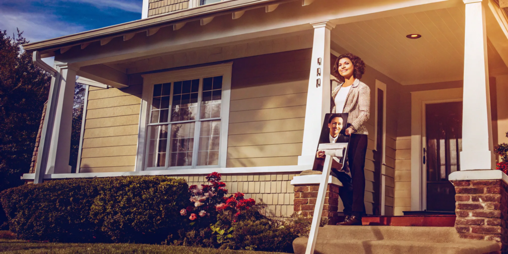 Woman selling her house as is by owner with a for sale sign on the porch.