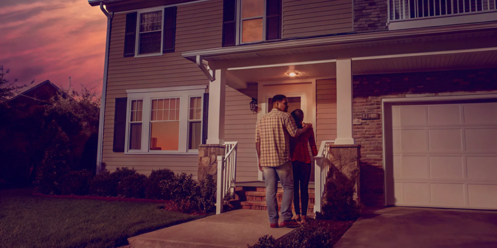 Couple standing in front of the inherited house they want to sell.