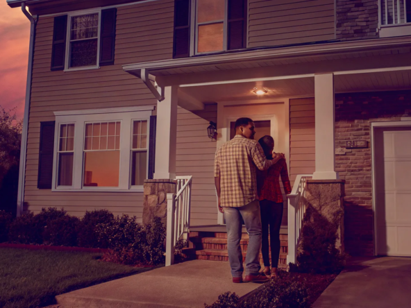 Couple standing in front of the inherited house they want to sell.