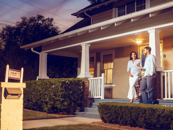 Couple on their porch with a for sale sign, learning how cash home buyers work.