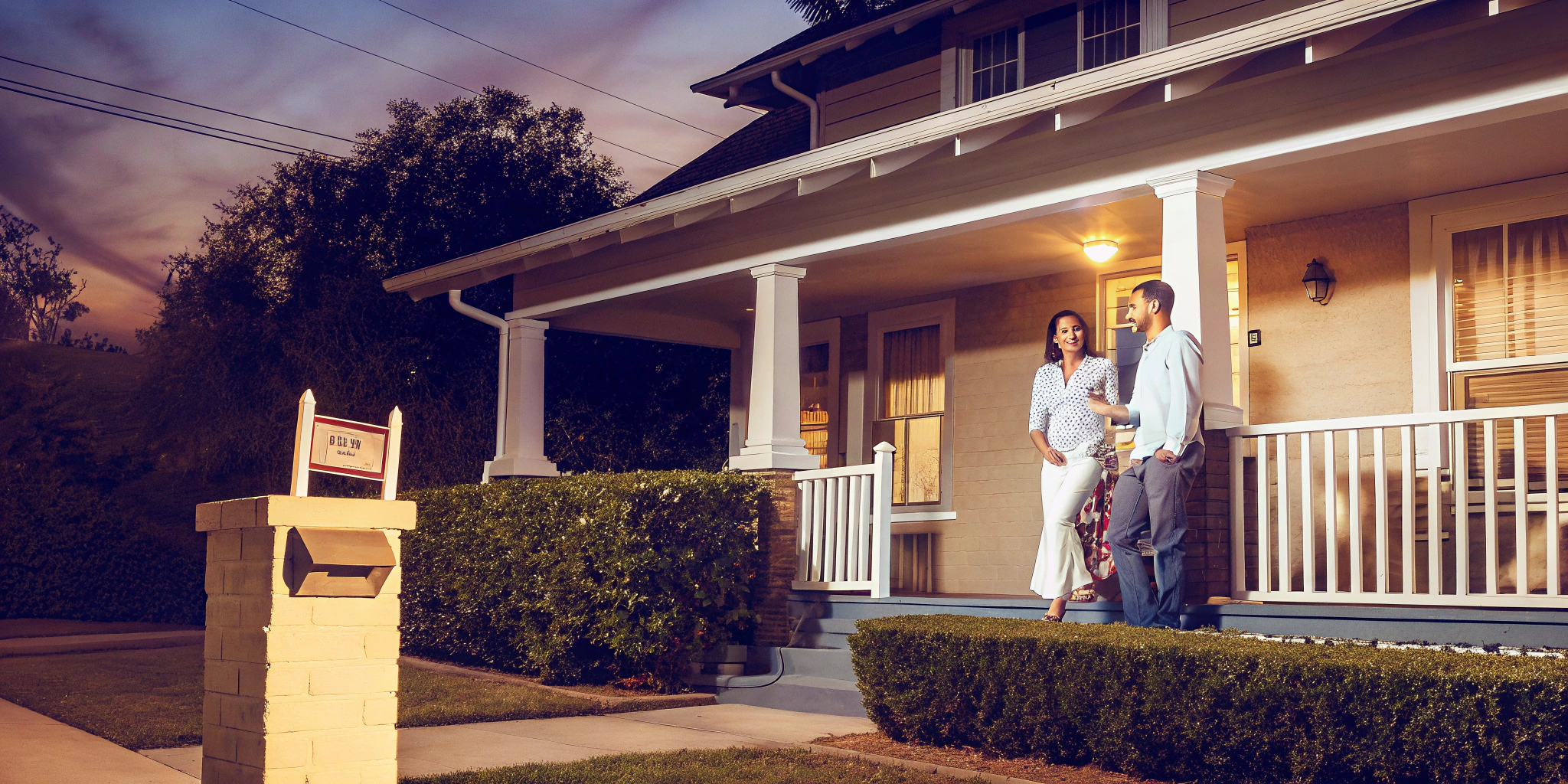 Couple on their porch with a for sale sign, learning how cash home buyers work.